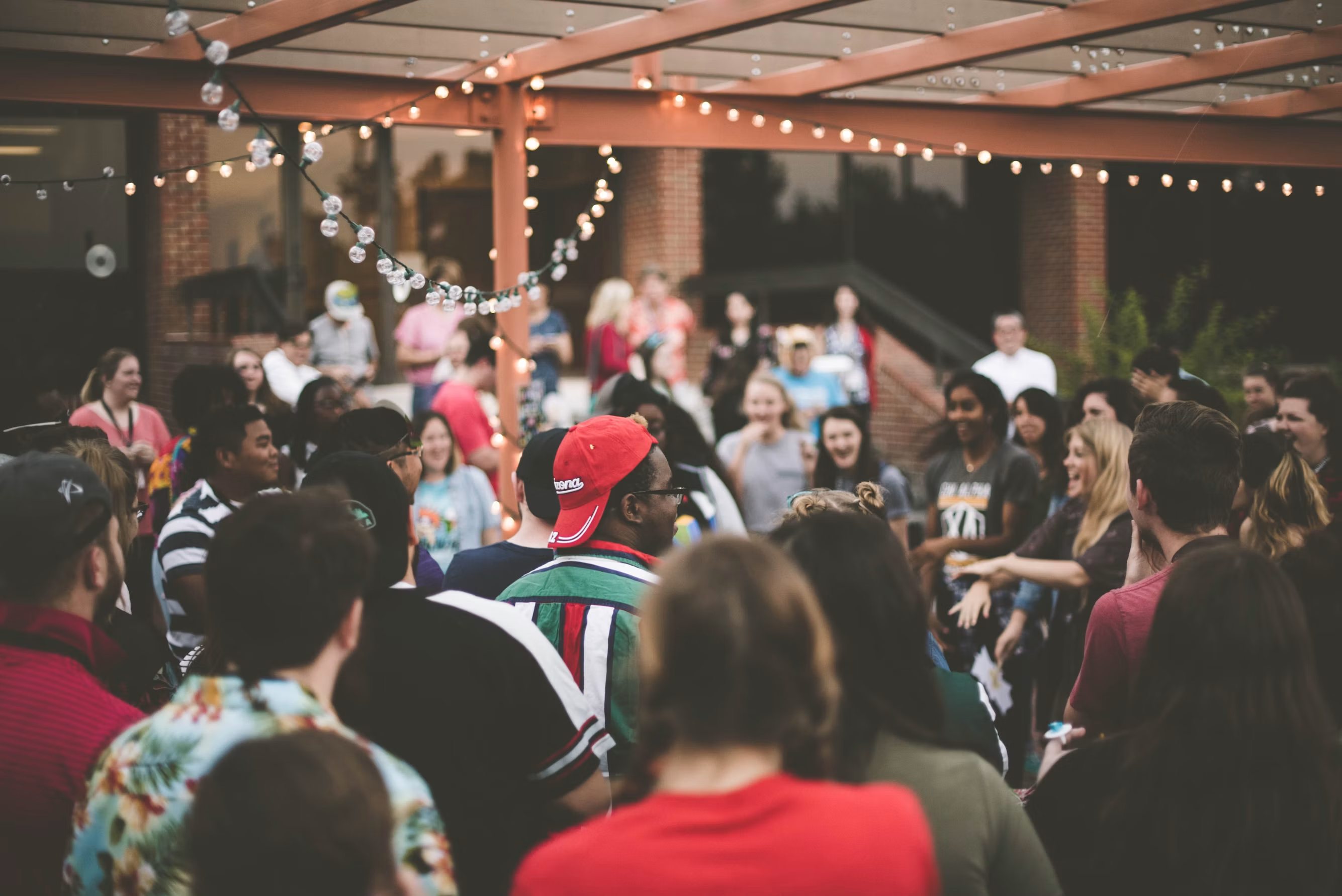 A lively queer community gathering under string lights in an outdoor venue